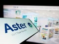 Mobile phone with logo of health company Aster DM Healthcare Limited on screen in front of business website.