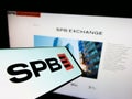 Mobile phone with logo of Russian financial marketplace SPB Exchange on screen in front of business website.