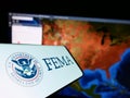 Mobile phone with seal of Federal Emergency Management Agency (FEMA) on screen in front of website.