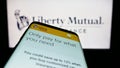 Mobile phone with web page of American insurance company Liberty Mutual Group on screen in front of logo.