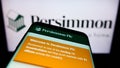 Mobile phone with webpage of British housebuilding company Persimmon plc on screen in front of business logo.