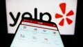 Mobile phone with webpage of US review platform company Yelp Inc. on screen in front of business logo.