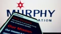 Mobile phone with website of American exploration company Murphy Oil Corporation on screen in front of logo.