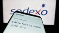 Mobile phone with website of French facility management company Sodexo S.A. on screen in front of logo.