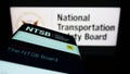 Mobile phone with website of US National Transportation Safety Board (NTSB) on screen in front of seal.