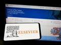 Person holding cellphone with logo of academic publishing company Elsevier on screen in front of business webpage.