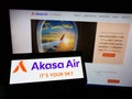 Person holding cellphone with logo of airline SNV Aviation Private Limited (Akasa Air) on screen in front of webpage.