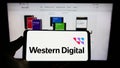 Person holding cellphone with logo of American company Western Digital Corporation (WDC) on screen in front of webpage.