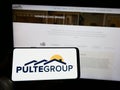 Person holding cellphone with logo of American home construction company PulteGroup Inc. on screen in front of webpage.
