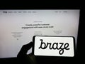 Person holding cellphone with logo of American marketing software company Braze Inc. on screen in front of webpage.