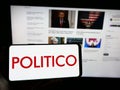 Person holding cellphone with logo of American political newspaper company Politico LLC on screen in front of webpage.