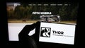 Person holding cellphone with logo of American RV manufacturing company Thor Industries Inc. on screen in front of webpage.