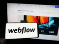 Person holding cellphone with logo of American web development software company Webflow Inc. on screen with website. Royalty Free Stock Photo
