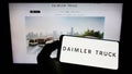 Person holding cellphone with logo of automotive company Daimler Truck Holding AG on screen in front of business webpage.