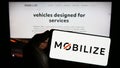 Person holding cellphone with logo of automotive mobility company Mobilize on screen in front of business webpage.