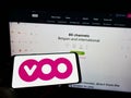 Person holding cellphone with logo of Belgian telecommunications company Voo S.A. on screen in front of business webpage.