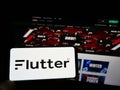 Person holding cellphone with logo of bookmaking company Flutter Entertainment plc on screen in front of Pokerstars website.