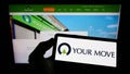 Person holding cellphone with logo of British company Your-Move.co.uk Limited on screen in front of business webpage.