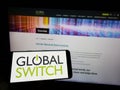 Person holding cellphone with logo of British data center company Global Switch Limited on screen in front of webpage.