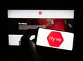 Person holding cellphone with logo of British event management company Hyve Group plc on screen in front of webpage.