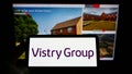 Person holding cellphone with logo of British housebuilding company Vistry Group plc on screen in front of webpage.