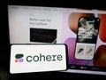 Person holding cellphone with logo of Canadian AI company Cohere Inc. on screen in front of business webpage.