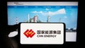 Person holding cellphone with logo of company China Energy Investment Corporation on screen in front of bsuiness webpage.