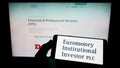 Person holding cellphone with logo of company Euromoney Institutional Investor plc on screen in front of business webpage.