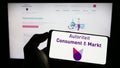 Person holding cellphone with logo of Dutch regulator Autoriteit Consument en Markt (ACM) on screen in front of webpage.