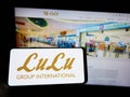 Person holding cellphone with logo of Emirati retail company LuLu Group International on screen in front of webpage.