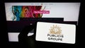 Person holding cellphone with logo of French advertising company Publicis Groupe S.A. on screen in front of webpage.