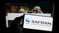 Person holding cellphone with logo of French aerospace company Safran S.A. on screen in front of business webpage. Royalty Free Stock Photo