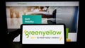 Person holding cellphone with logo of French energy company GreenYellow SAS on screen in front of business webpage.