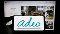 Person holding cellphone with logo of French retail company Adeo S.A. on screen in front of business webpage.