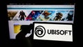 Person holding cellphone with logo of French video game company Ubisoft Entertainment SA on screen in front of web page. Royalty Free Stock Photo