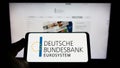 Person holding cellphone with logo of German central bank Deutsche Bundesbank on screen in front of webpage.