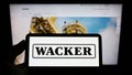Person holding cellphone with logo of German chemical company Wacker Chemie AG on screen in front of business webpage.