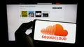 Person holding cellphone with logo of German music sharing company SoundCloud on screen in front of business webpage.