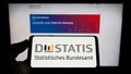 Person holding cellphone with logo of German Statistisches Bundesamt (Destatis) on screen in front of webpage.