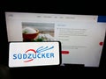 Person holding cellphone with logo of German sugar production company SÃÂ¼dzucker AG on screen in front of business webpage.