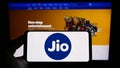 Person holding cellphone with logo of Indian telecommunications company Reliance Jio on screen in front of webpage.