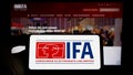 Person holding cellphone with logo of Internationale Funkausstellung Berlin (IFA) on screen in front of webpage. Royalty Free Stock Photo