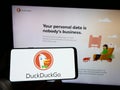 Person holding cellphone with logo of Internet search engine DuckDuckGo (DDG) on screen in front of business webpage.