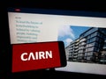 Person holding cellphone with logo of Irish housebuilding company Cairn Homes plc on screen in front of business webpage.