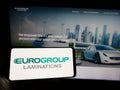 Person holding cellphone with logo of Italian company EuroGroup Laminations SpA on screen in front of business webpage.