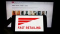 Person holding cellphone with logo of Japanese retail company K.K. Fast Retailing on screen in front of Uniqlo website.