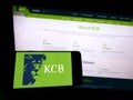 Person holding cellphone with logo of Kenyan financial company KCB Group Limited on screen in front of business webpage.