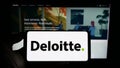 Person holding cellphone with logo of professional services company Deloitte on screen in front of business webpage.