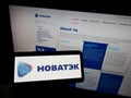 Person holding cellphone with logo of Russian natural gas company Novatek on screen in front of business webpage.