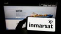 Person holding cellphone with logo of satellite company Inmarsat Global Limited on screen in front of business webpage. Royalty Free Stock Photo